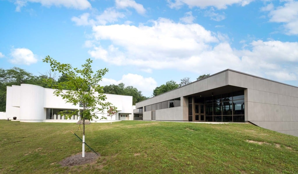 Modern low-rise building with large windows beside a grassy lawn and young tree.