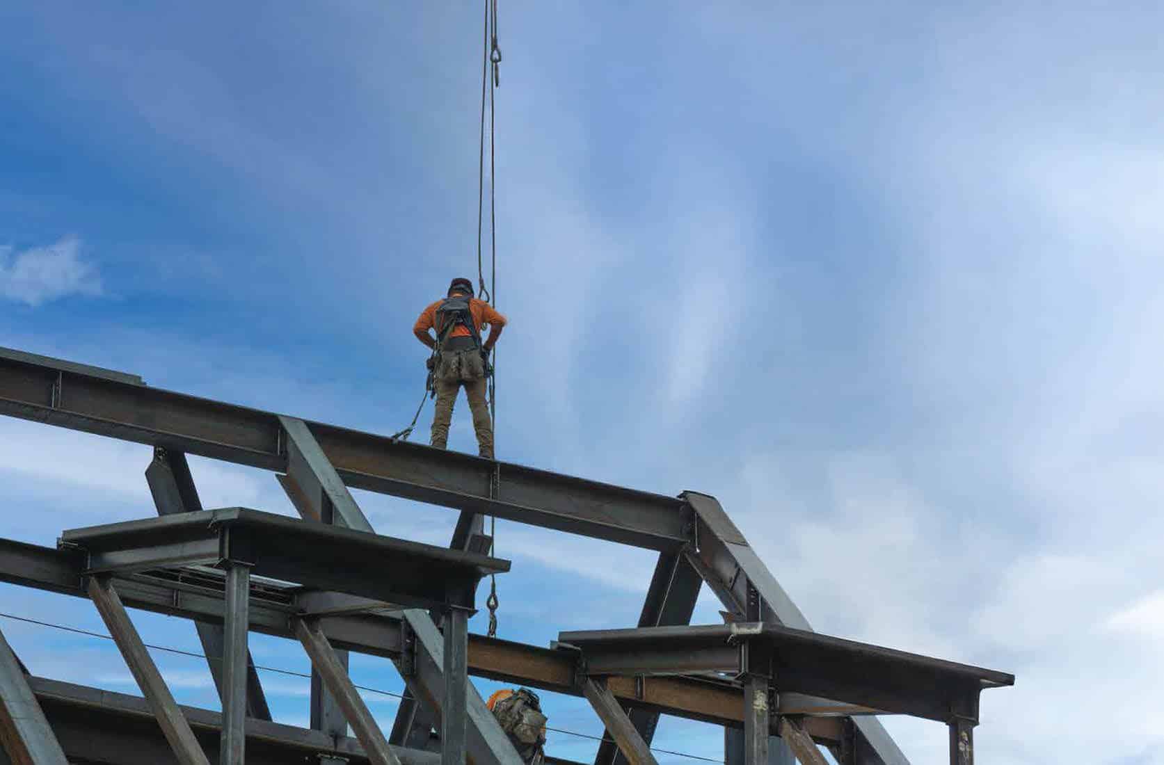 Man standing on steel beam on top of structure with safety gear