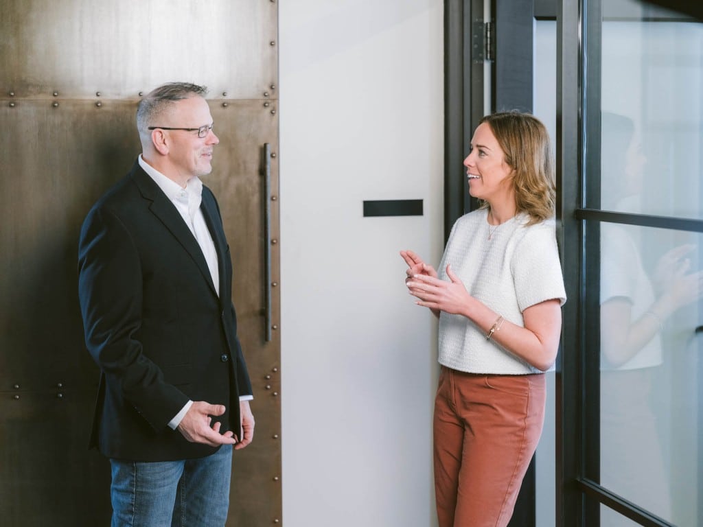 Two colleagues talking in a modern office hallway.