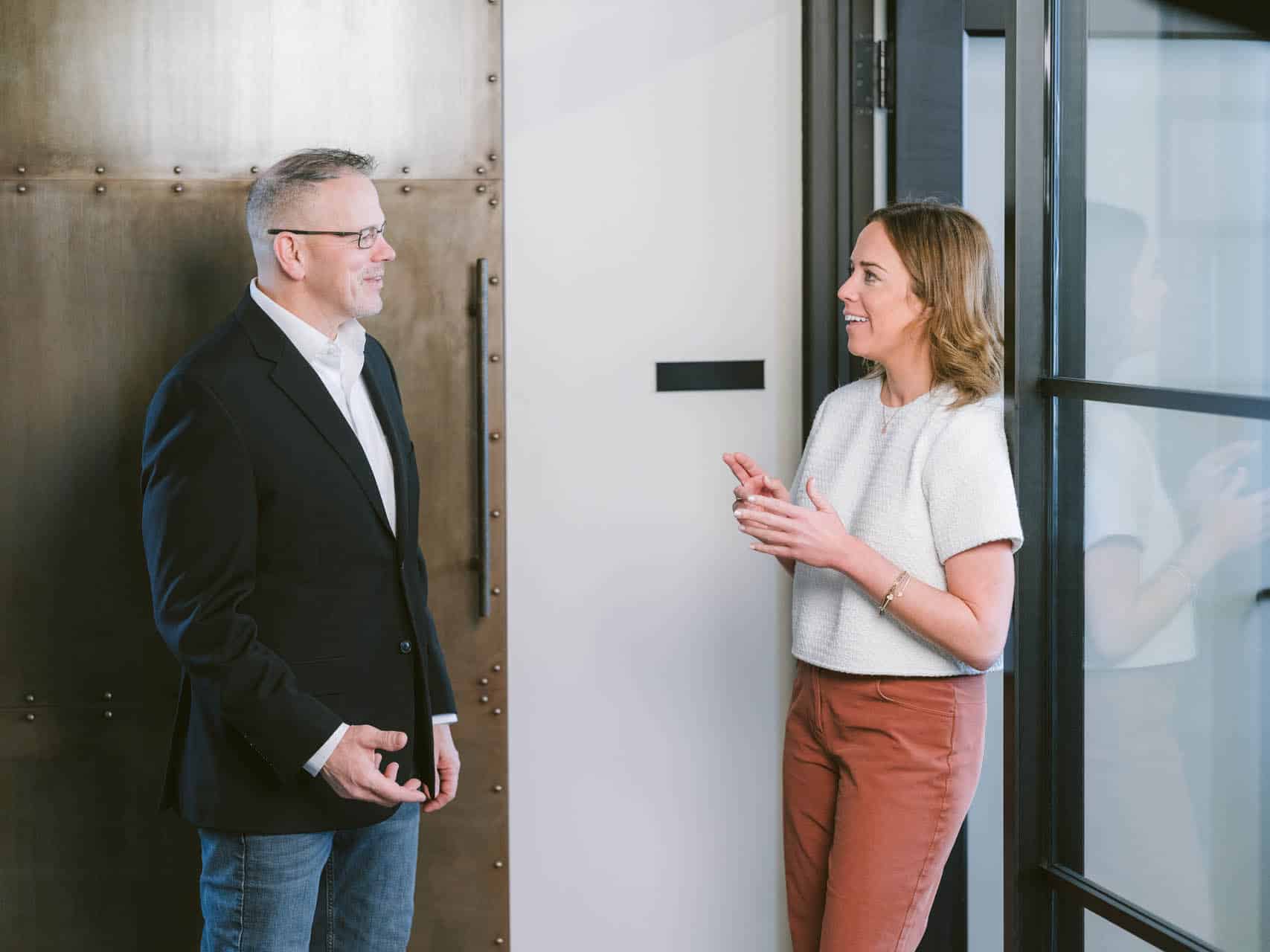 Two colleagues talking in a modern office hallway.