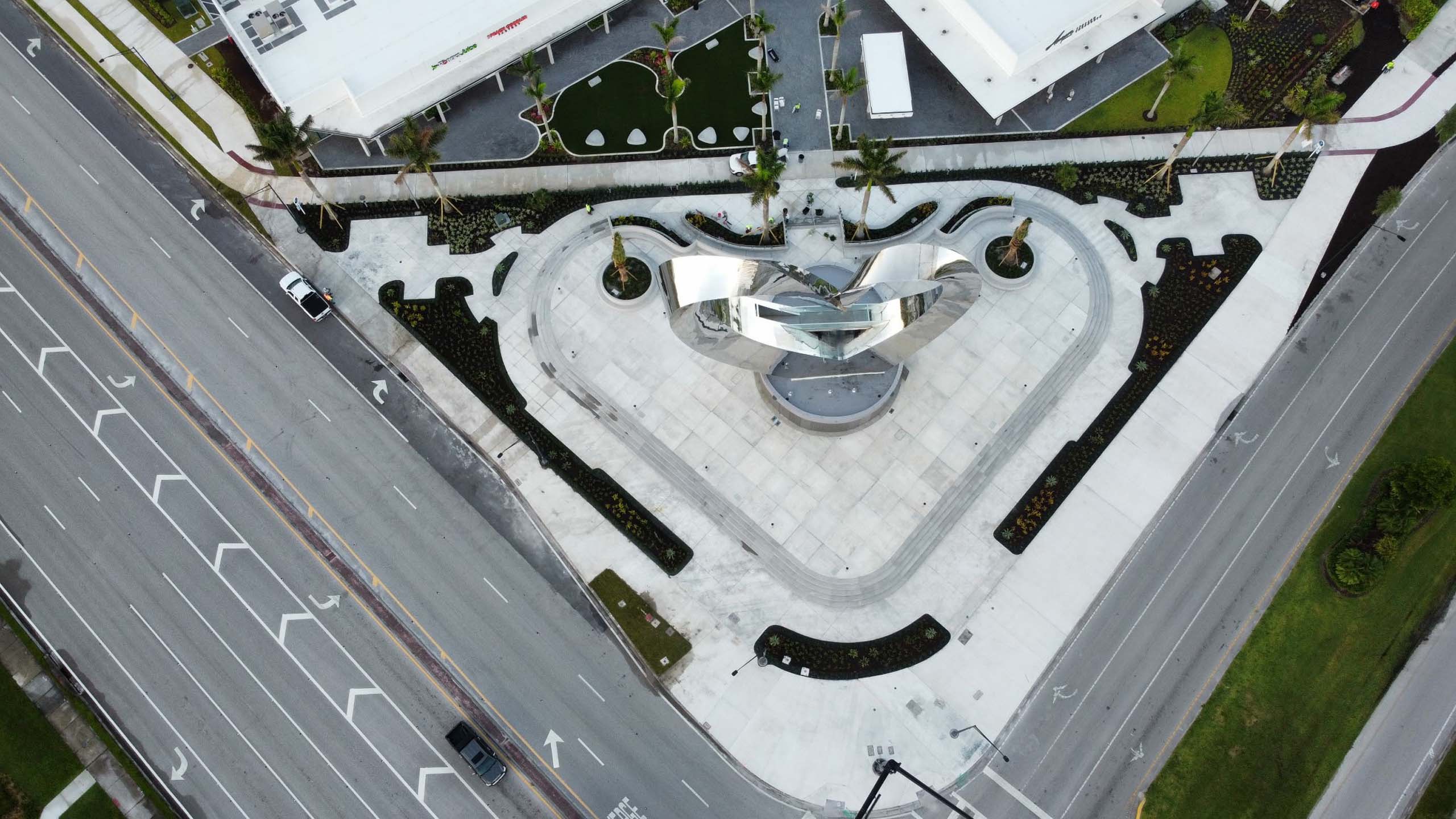 Lit triangular plaza with a reflective metal sculpture at the center in the day time.