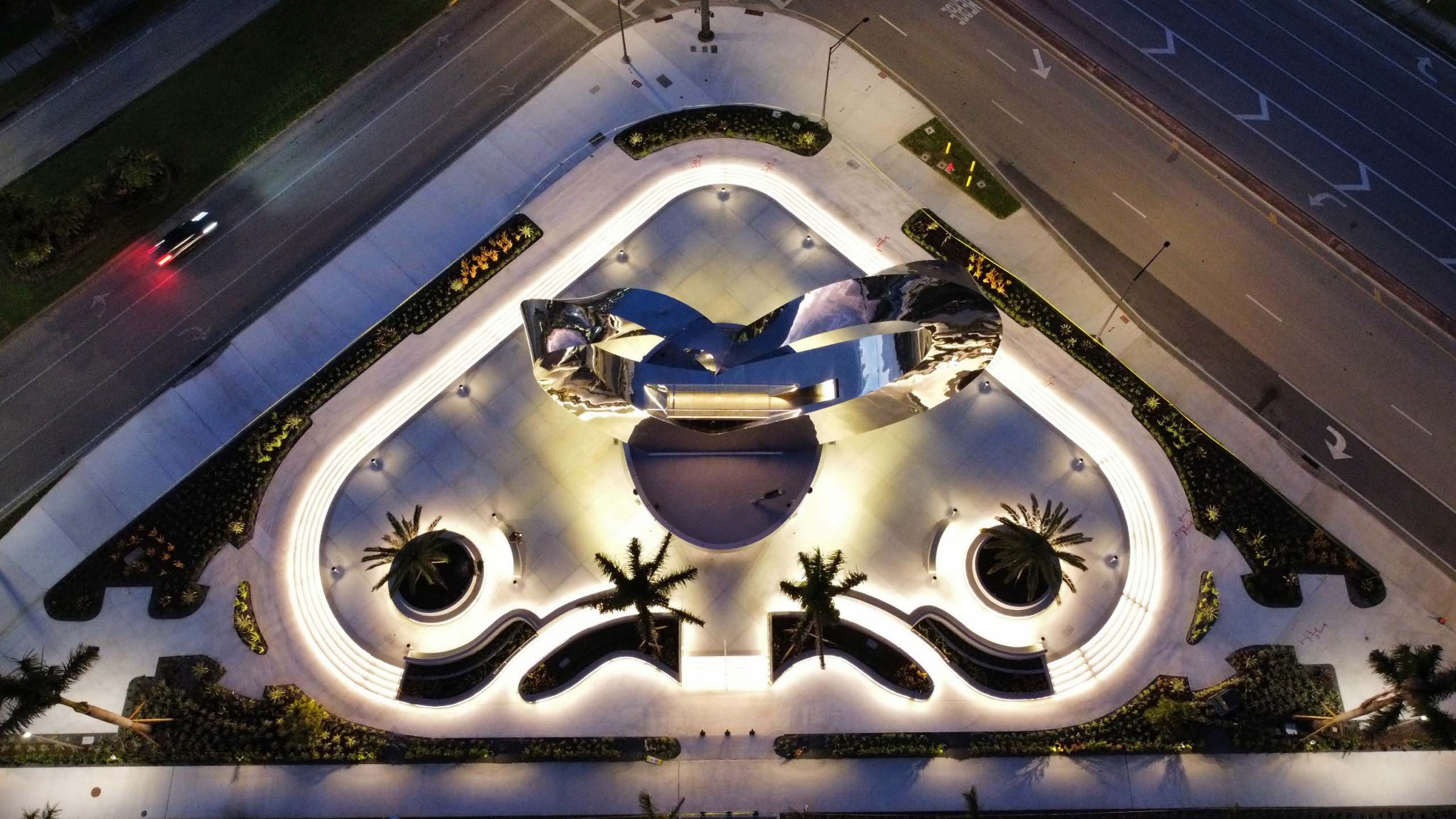 Lit triangular plaza with a reflective metal sculpture at the center.