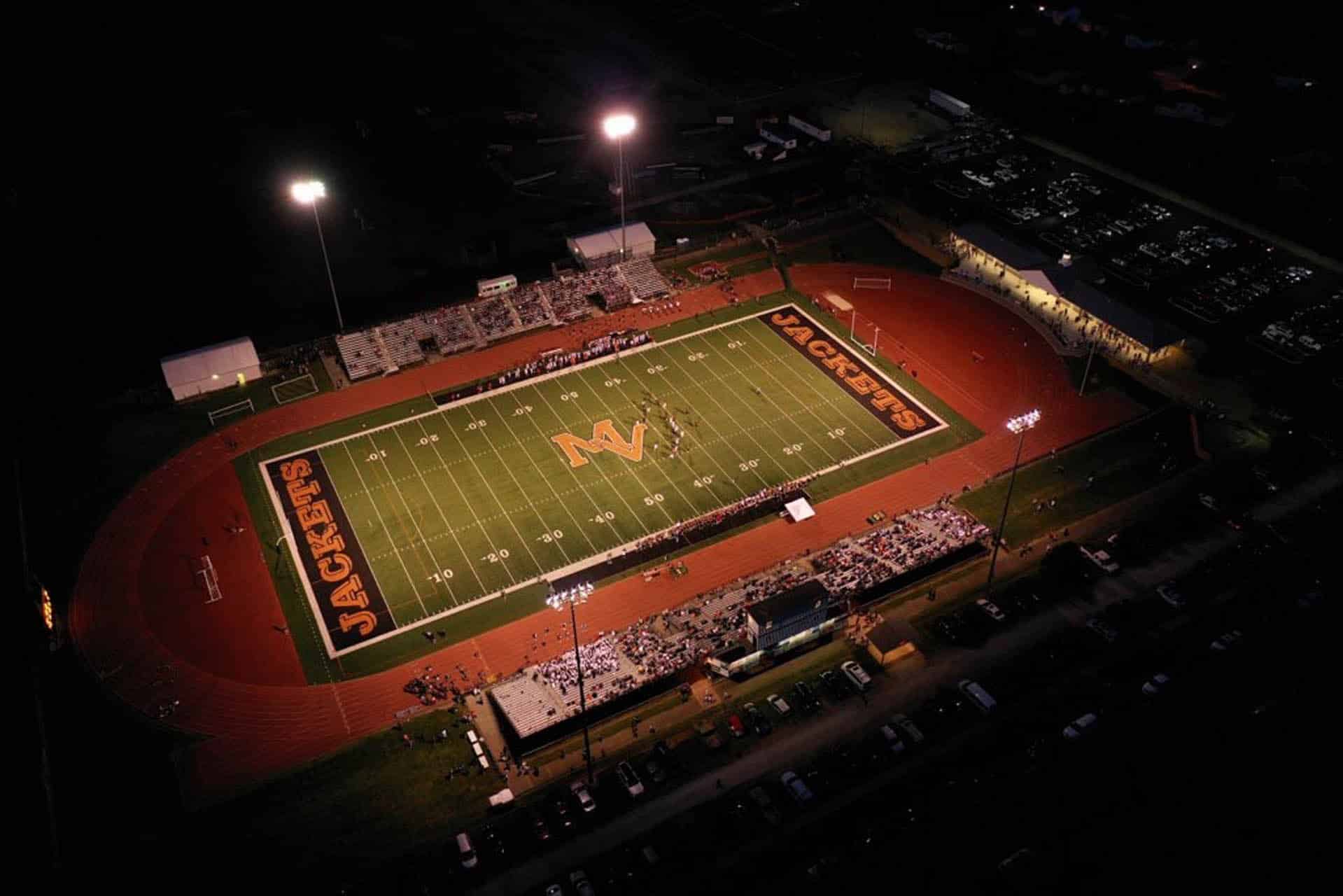 Aerial view of a lit high school football field at night.