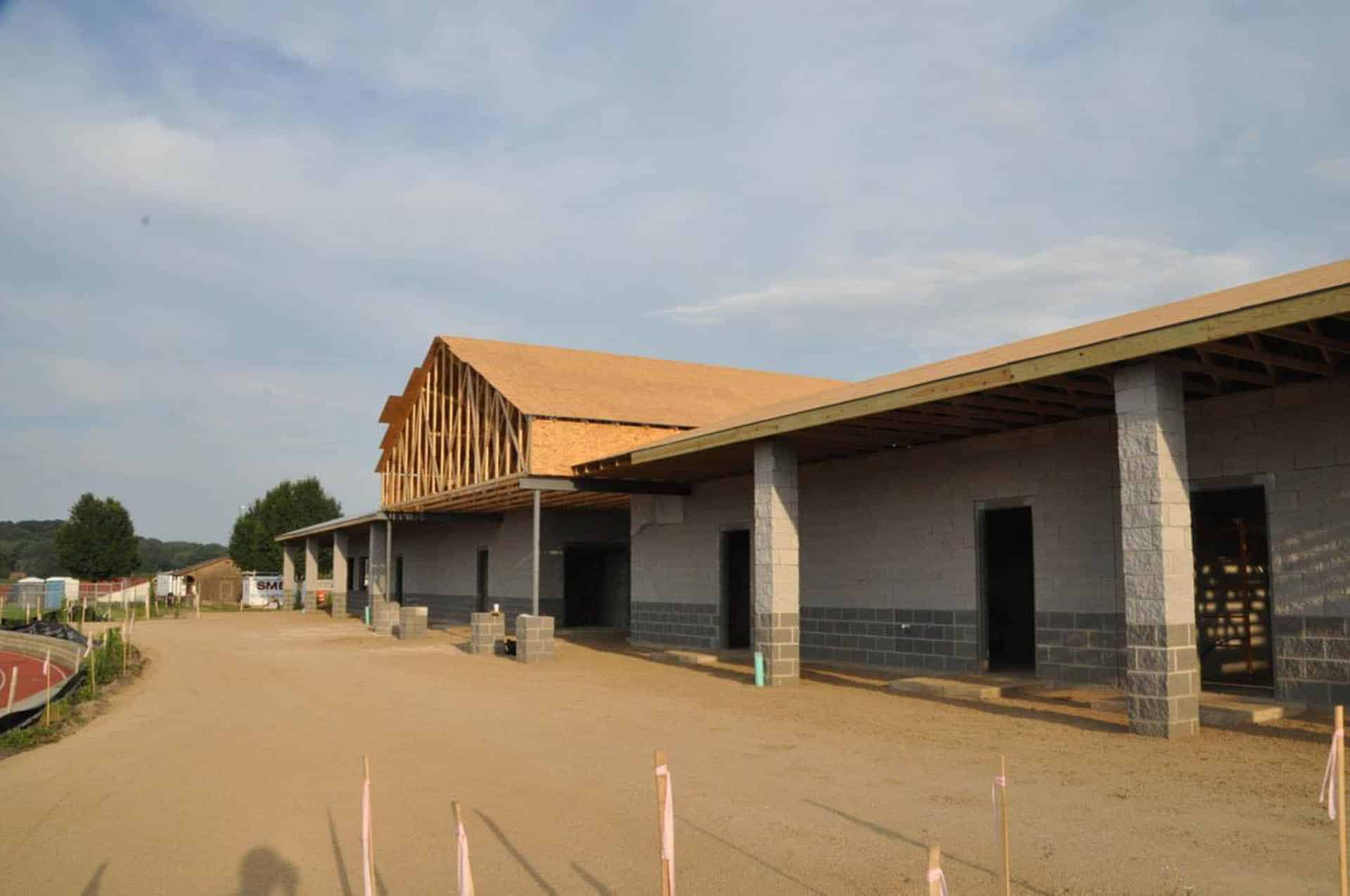 Exterior view of a partially framed pavilion under construction with concrete block walls and a dirt forecourt.