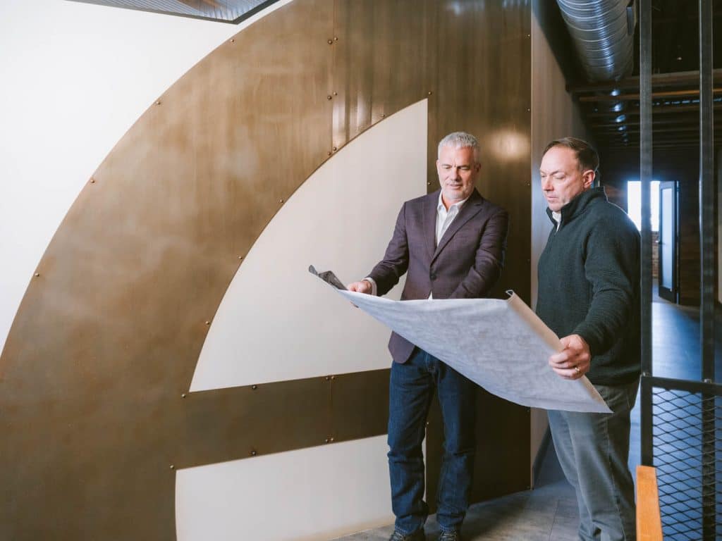 Two colleagues reviewing construction plans in an industrial hallway.