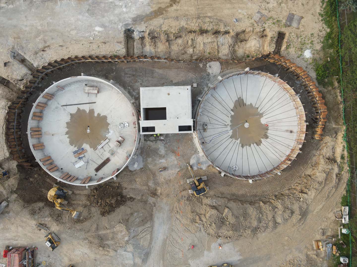 Aerial view of two large circular concrete tanks under construction connected by a central structure.